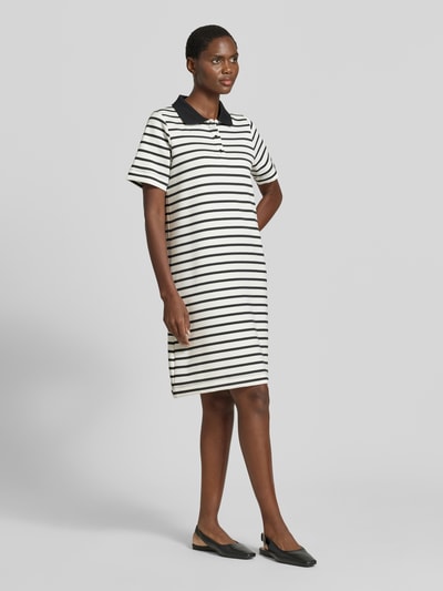 Frauenmodel trägt Knielanges Polokleid mit kurzer Knopfleiste Modell 'BARNI' von Soyaconcept im Material-Mix mit Modal-Anteil, Gerader-Schnitt, Polokragen, Knielänge, Brustweite 50 cm, Rückenlänge 50 cm, Ärmellänge 24 cm, schwarze Streifen auf weißem Grund, glatte Textur. Ganzkörperansicht von vorne.