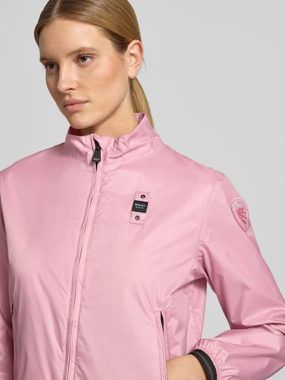 Kobiece modelka nosi kurtkę Jacke mit Zweiwege-Reißverschluss Modell 'ANNABEL' od Blauer Usa, krój regular fit, stójka, detale z logo, kieszenie zapinane na zamek błyskawiczny, różowy kolor, gładka faktura, zamek błyskawiczny dwustronny, szerokość ramion w rozmiarze S: 42 cm, długość tyłu: 58 cm, szerokość w rozmiarze S: 50 cm, długość rękawów: 60 cm, zbliżenie na górną część ciała.