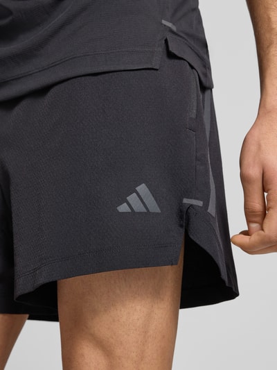 Männermodel trägt Regular Fit Sport-Shorts mit Logo-Print von adidas Training, Optik: Unifarben, Nahaufnahme Oberschenkel. Passform Regular-Fit, Applikation: Logo-Print, Verschluss: Tunnelzug innen, Bundabschluss: elastisch, Funktion: schnelltrocknend, schweißableitend, seitliche Reißverschlusstasche.