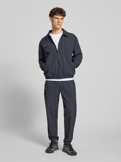 Männermodel trägt Trackpants mit Reißverschlusstaschen Modell 'HALO MOVE' von HALO in Dunkelblau, Material-Mix mit Stretch-Anteil, Regular-Fit, Label-Print, Ganzkörperansicht von vorne.