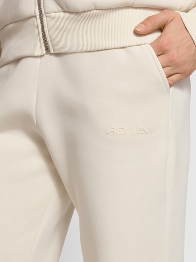 Frauenmodel trägt Basic Sweatpant mit Bündchen am Saum und seitlichen Taschen von Review aus Baumwoll-Mix, Logo-Stickerei, Nahaufnahme Oberkörper.