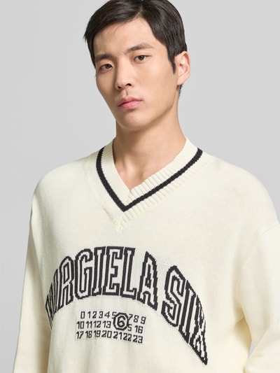 Männermodel trägt Pullover in Strick-Optik von MM6 Maison Margiela in Elfenbein mit V-Ausschnitt und Logo-Print, Nahaufnahme Oberkörper.