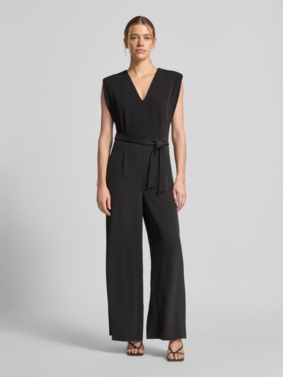 Frauenmodel trägt Jumpsuit mit V-Ausschnitt und Bindegürtel von Comma aus schwarzem Material-Mix mit Stretch-Anteil, Regular-Fit, Ganzkörperansicht von vorne. Rückenlänge 141 cm, Brustweite 36 cm, Gesamtlänge 144 cm, Innenbeinlänge 80 cm bei Größe 36.