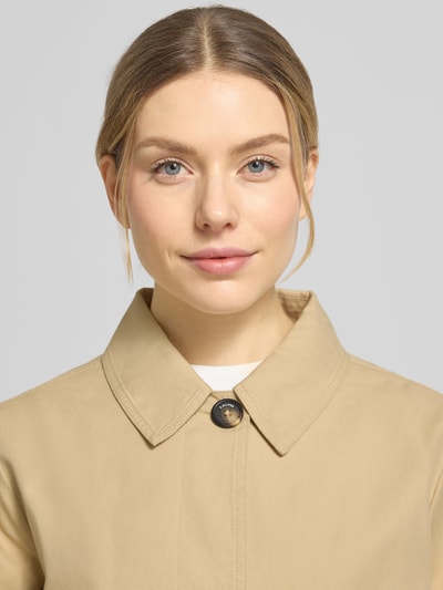 Vrouwenmodel draagt Regular Fit Trenchcoat aus Baumwoll-Lyocell-Mix van s.Oliver RED LABEL in effen beige twill, close-up bovenlichaam.
