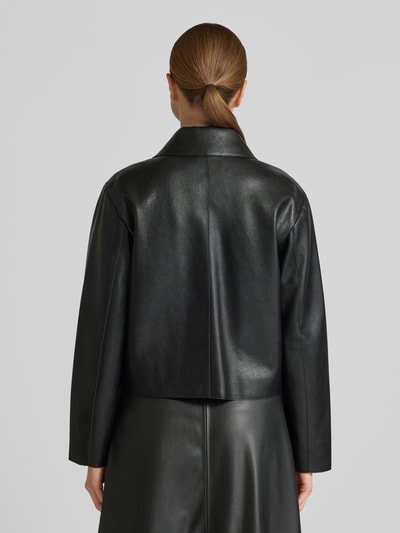 Frauenmodel trägt Jacke in Leder-Optik Modell 'SABINA' von Mango, schwarz, Regular-Fit, Hemdblusenkragen, Knopfleiste, Pattentaschen, Rückenlänge 52 cm, Schulterbreite 41 cm, Brustweite 48 cm, Ärmellänge 58 cm, Ganzkörperansicht Rückansicht.