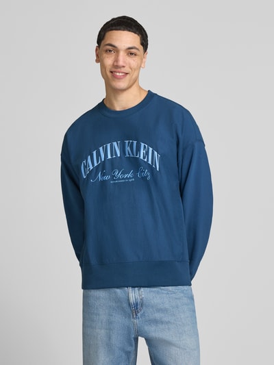 Männermodel trägt Sweatshirt mit Label-Stitching von Calvin Klein Jeans in Blau, Baumwoll-Mix, Gerader-Schnitt, Rundhalsausschnitt, überschnittene Schultern, Rückenlänge 70 cm, Ärmellänge 70 cm, Ganzkörperansicht von vorne.