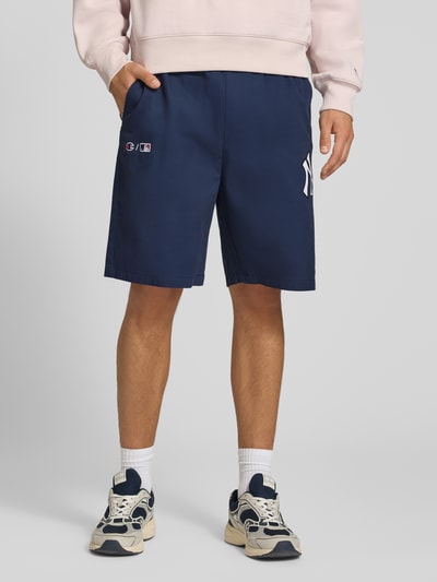 Männermodel trägt Relaxed Fit Shorts aus reiner Baumwolle von Champion, marineblau, elastischer Bund, Logo-Stitching, Ganzkörperansicht von vorne.