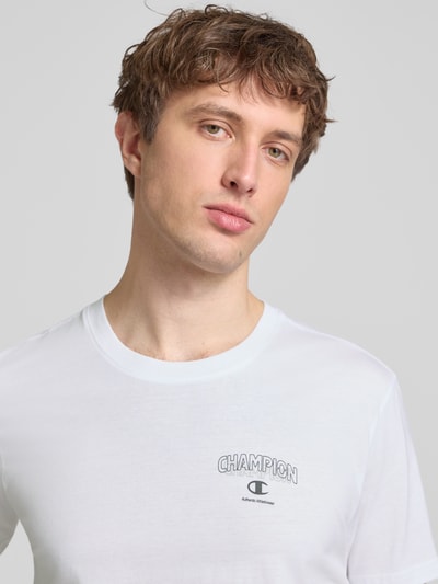 Männermodel trägt T-Shirt mit Logo und Rundhalsausschnitt von CHAMPION aus reiner Baumwolle in Weiß, Regular Fit, Nahaufnahme Oberkörper.