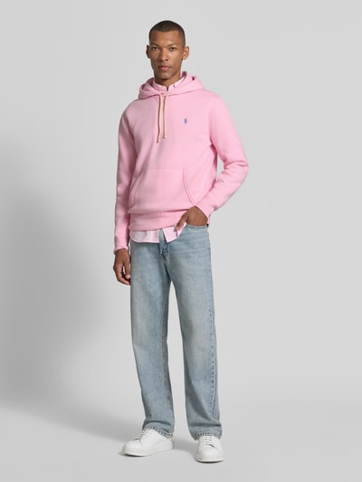 Mannelijk model draagt Regular Fit Hoodie uit katoenmix van Polo Ralph Lauren in lichtroze, met lichtblauwe jeans, Ganzkörperansicht van voren.