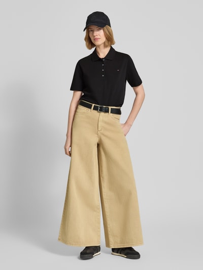 Frauenmodel trägt Regular Fit Poloshirts aus Baumwoll-Mix von Tommy Hilfiger in Unifarben Schwarz mit kurzem Arm, Logo-Stitching, Polokragen und V-Ausschnitt, Material Piqué, Ganzkörperansicht von vorne.