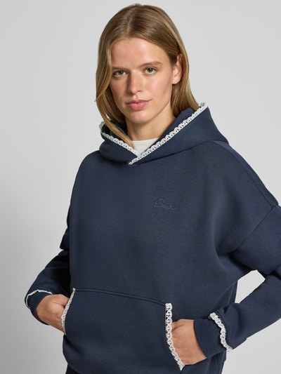 Frauenmodel trägt Hoodie mit Häkelspitzenbesatz von REVIEW, dunkelblau, Baumwollmischung, Logo-Print, Kängurutasche, Nahaufnahme Oberkörper.