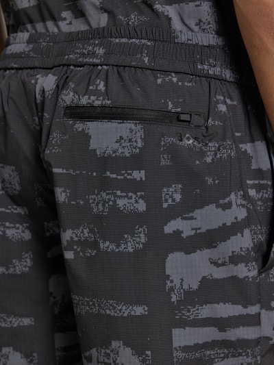 Männermodel trägt Regular Fit Shorts mit Allover-Muster Modell 'Globe AOP' von BOSS Green, Camouflage-Optik, Detailaufnahme Gesäßtasche.