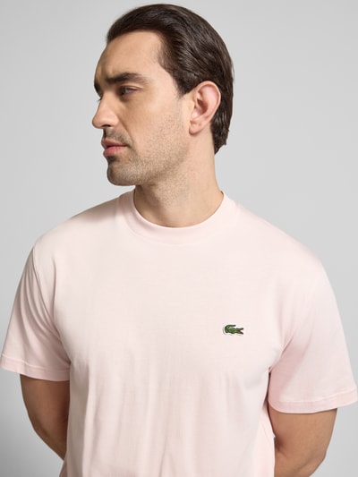 Männermodel trägt Regular Fit T-Shirt aus reiner Baumwolle von Lacoste in effen lichtroze, label stitching, logo-patch, ronde hals, korte mouw, Nahaufnahme Oberkörper.