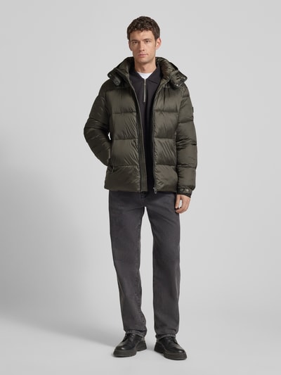 Męski model nosi Kurtka pikowana z kieszeniami zapinanymi na zamek błyskawiczny od JOOP! Collection, prosty krój, kaptur, długość tyłu 75 cm, szerokość ramion 49 cm, szerokość klatki piersiowej 45 cm, długość rękawów 69 cm, całość w odcieniach oliwkowej zieleni, całkowity widok z przodu.