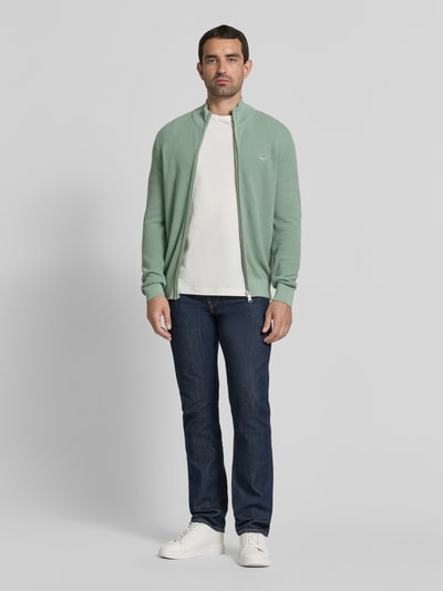 Męski model nosi Regular Fit Strickjacke aus reiner Baumwolle von GANT w kolorze jasnej zieleni, prosta forma, gładka tekstura, Ganzkörperansicht von vorne.