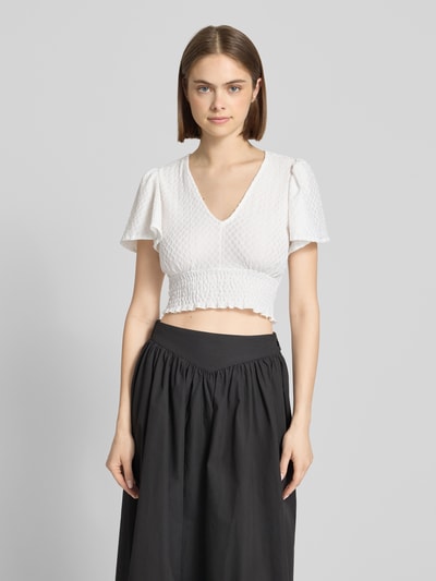 Vrouwenmodel draagt Regular fit crop top met structuurpatroon model 'HANNAH' van Only, wit met gesmokte borstband, V-hals, unilook, vlindermouwen, korte mouwen en smokrand bij de zoom, close-up bovenlichaam vooraanzicht.