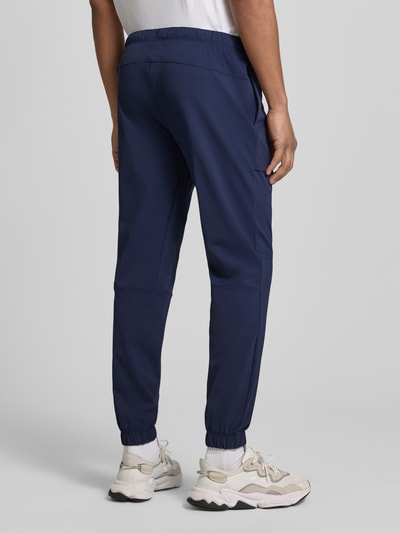 Männermodel trägt Slim Fit Jogger mit elastischem Bund von Fabletics, Elastischer-Material-Mix, Eingrifftaschen, Ganzkörperansicht Rückansicht.