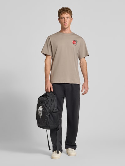 Männermodel trägt T-Shirt aus reiner Baumwolle Modell 'Gear Up Get Out' von The North Face in Beige mit Logo-Print, Ganzkörperansicht von vorne. Regular Fit, kurzärmliges Design, Rundhalsausschnitt, Rückenlänge bei Größe M 68 cm.