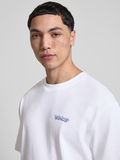 Männermodel trägt Relaxed Fit T-Shirt aus reiner Baumwolle Modell 'FRED DU MARTIN' von Only & Sons, unifarben weiß, Motiv-Print, Nahaufnahme Oberkörper.
