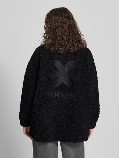 Frauenmodel trägt Jacke aus Teddyfell mit Stehkragen von Karo Kauer, oversized, schwarz, weiche Textur, Rückenansicht, Ganzkörperansicht Rückansicht.