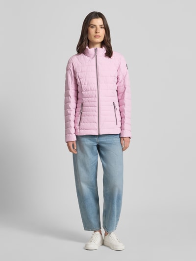 Kobiece model nosi kurtkę pikowaną z zamkiem błyskawicznym i kieszeniami model 'GS 111' od G.I.G.A. DX, krój slim fit, stójka, długość tyłu w rozmiarze 36: 67 cm, szerokość ramion w rozmiarze 36: 38 cm, szerokość klatki piersiowej w rozmiarze 36: 49 cm, długość rękawów w rozmiarze 36: 65 cm, różowy kolor, prosty dół, cała sylwetka z przodu.