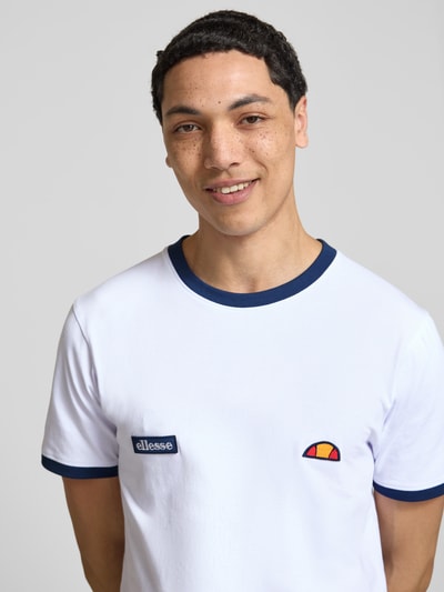 Męski model nosi T-Shirt mit Logo- und Label-Patch Modell 'RINGETTO' od Ellesse, biała bawełna, krój regular fit, okrągły dekolt, prosty fason, długość tyłu w rozmiarze M: 72 cm, zbliżenie na górną część ciała