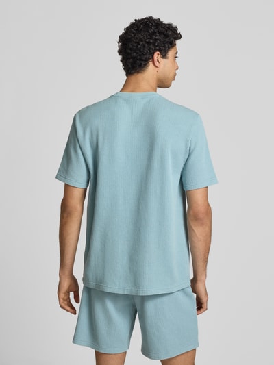 Männermodel trägt T-Shirt mit Strukturmuster und Label-Stitchings von CHAMPION, Baumwoll-Mix, hellblau, Rückansicht Ganzkörperansicht.