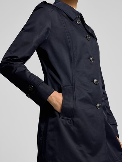 Frauenmodel trägt Trenchcoat mit Ärmelriegeln von Fuchs Schmitt in Dunkelblau, sichtbare Knopfleiste und Eingrifftaschen, Nahaufnahme Oberkörper.