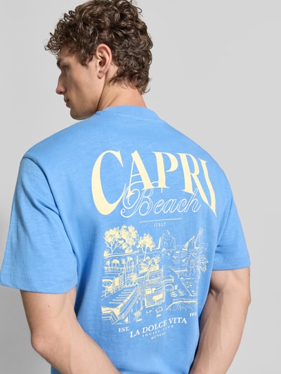 Männermodel trägt T-Shirt aus Baumwolle mit rückseitigem Print von MCNEAL in Blau mit Relaxed-Fit und Rundhalsausschnitt, Rückenlänge 62 cm, Ganzkörperansicht Rückansicht.