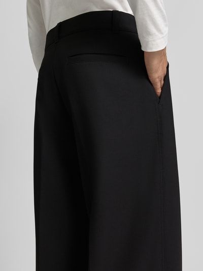 Männermodel trägt High Waist Bundfaltenhose mit Bügelfalten von HUGO, unifarbenes Design, krój wide leg, Knopf und ukryty zamek, Ganzkörperansicht Rückansicht.