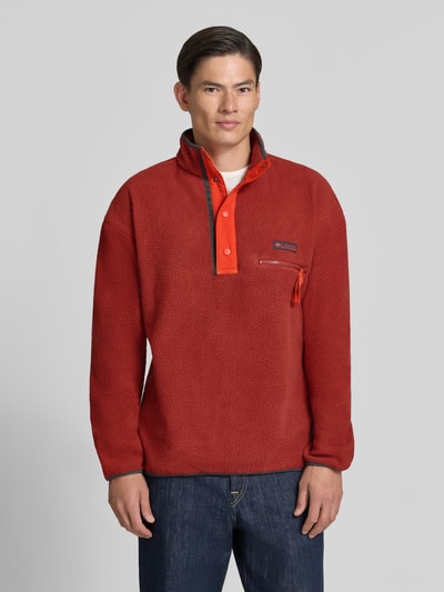 Männermodel trägt Fleecepullover mit Label-Patch Modell 'Helvetia™ II' von Columbia in Rot, Stehkragen, Knopfleiste, Brusttasche, Ganzkörperansicht von vorne.