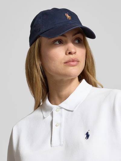Kobiece model nosi Boxy Fit Poloshirt mit Label-Stitching von Polo Ralph Lauren z bawełny, biały kolor, kołnierzyk polo, listwa guzikowa, wyhaftowane logo, długość tyłu 52 cm dla rozmiaru S, zbliżenie na górną część ciała.