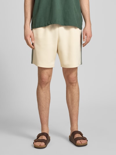 Männermodel trägt Regular Fit Sweatshorts mit elastischem Bund Modell 'RIBER' von Only & Sons, cremefarben, mit Kontraststreifen, unifarben, Eingrifftaschen, Nahaufnahme Oberschenkelansicht.