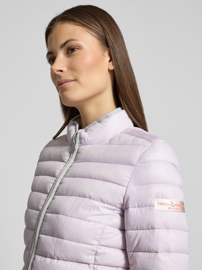 Kobieta nosi Steppjacke mit Reißverschlusstaschen Modell 'SISTER JUDY' von Frieda & Freddies, kolor jasnofioletowy, krój slim fit, stójka, zamek błyskawiczny, kieszenie na zamek, długość tyłu w rozmiarze 36: 56 cm, szerokość ramion w rozmiarze 36: 41 cm, szerokość w biuście w rozmiarze 36: 47 cm, długość rękawa w rozmiarze 36: 61 cm, tkanina pikowana, matowe wykończenie; zbliżenie górnej części ciała z przodu.