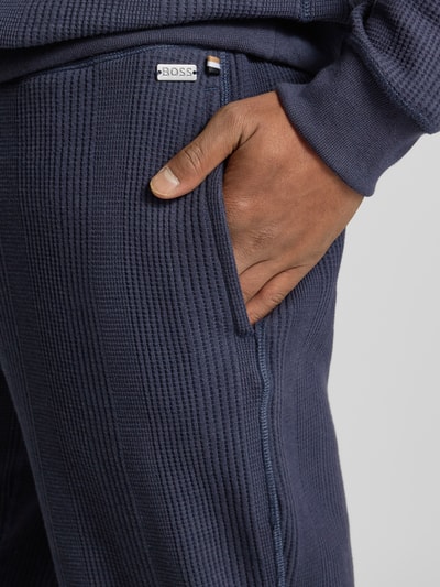 Männermodel trägt Comfort Fit Sweatpants aus Baumwoll-Mix Modell 'STRUCTURE PANTS' von BOSS, Optik: Unifarben, Struktur, Label-Applikation, seitliche Eingrifftaschen, Materialverarbeitung: Jacquard, Nahaufnahme seitlich