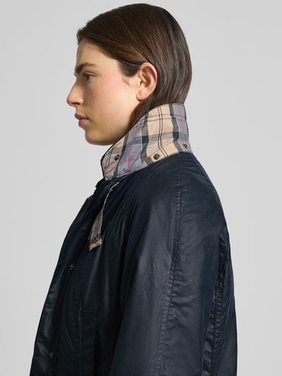 Kobiece modelka nosi Wachsjacke aus reiner Baumwolle od Barbour, granatowy kolor, krój regular fit, wodoodporna, delikatna faktura, zdjęcie z profilu, półzbliżenie na górną część ciała.