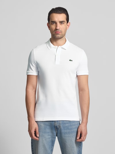 Männermodel trägt Slim Fit Poloshirt aus reiner Baumwolle von Lacoste, Optik: Unifarben, Logo-Stitching, Ganzkörperansicht von vorne.