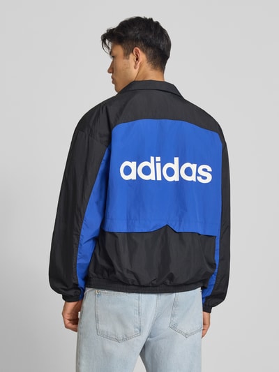 Männermodel trägt Regular Fit Trainingsjacke im Two-Tone-Design Modell 'MUC TT' von adidas Originals in Blau und Schwarz, Ganzkörperansicht Rückansicht.