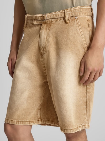 Männermodel trägt Relaxed Fit Jeansshorts aus Baumwolle von Don’t Waste Culture im Used-Look mit D-Ring-Verschluss, Eingriff- und Gesäßtaschen, in heller Sandfarbe, Nahaufnahme Oberschenkel.