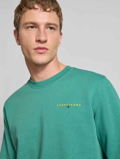 Männermodel trägt Regular Fit Sweatshirt aus Baumwoll-Mix Modell 'LINEAR CREW' von Tommy Jeans in Optik: Unifarben, Nahaufnahme Oberkörper.