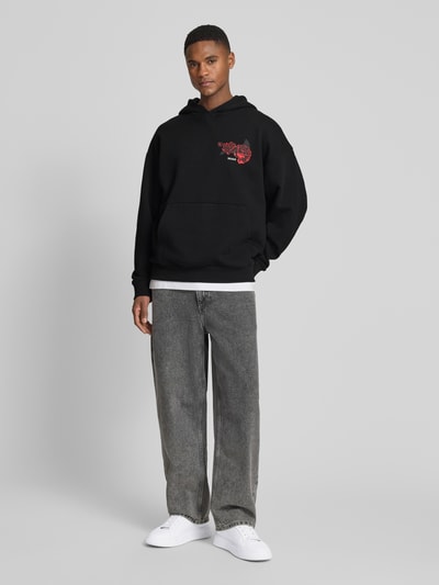 Männermodel trägt Regular Fit Hoodie aus reiner Baumwolle Modell 'DAGETHOOD' von HUGO in Schwarz, Optik: Unifarben, Motiv-Print, Kängurutasche, Sweat, Langarm, Kapuze, Label-Stitching, Ganzkörperansicht von vorne.