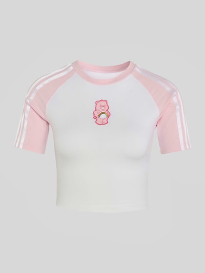 Frauenmodel trägt Slim Fit T-Shirt aus reiner Baumwolle mit Patch von adidas Originals, weiß-rosa mit Logo, Nahaufnahme Oberkörper.