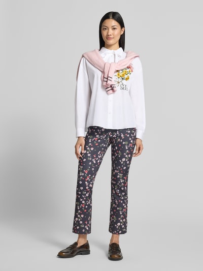 Frauenmodel trägt Relaxed Fit Hemdbluse aus reiner Baumwolle von Marc Cain, weiß mit Logo-Print und Brusttasche, Ganzkörperansicht von vorne.