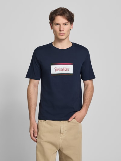 Männermodel trägt Regular Fit T-Shirt mit Logo-Print Modell 'Buster' von JACK & JONES in Dunkelblau aus Reine Baumwolle, Ganzkörperansicht von vorne. Rückenlänge bei Größe M: 71 cm.