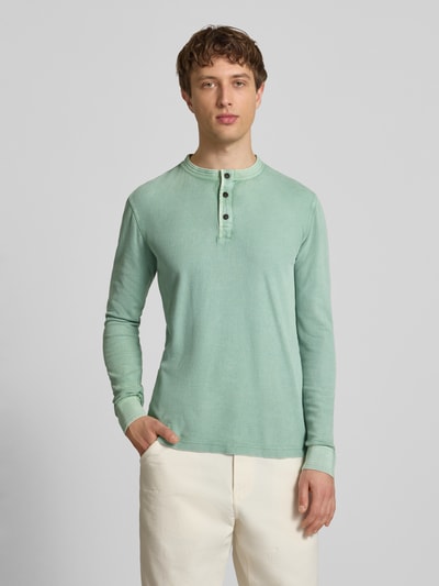 Męski model nosi Longsleeeve mit Knopfleiste od Superdry, czysta bawełna, krój regular fit, okrągły dekolt, długość tyłu w rozmiarze M: 72 cm, pastelowa zieleń, gładka tekstura, widok całej sylwetki z przodu.
