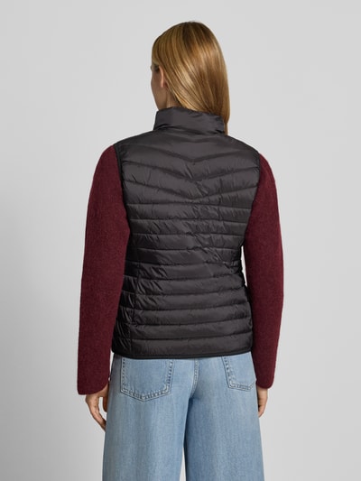 Vrouwenmodel draagt bodywarmer in stiksels van FUCHS SCHMITT, getailleerde pasvorm, opstaande kraag, tweewegritssluiting, ruglengte maat 36: 55 cm, schouderbreedte maat 36: 39 cm, borstwijdte maat 36: 48 cm, zwart met bordeaux, doorgestikte structuur, volledige achteraanzicht.