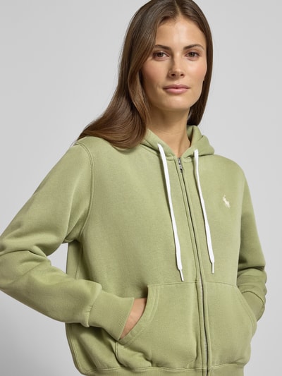 Kobiece modelka nosi bluzę rozpinaną z kapturem od Polo Ralph Lauren, mieszanka bawełny, luźny krój, zamek błyskawiczny, wyhaftowane logo, wpuszczane kieszenie, prążkowane wykończenia, jasna zieleń, gładka tekstura. Zbliżenie na górną część ciała.