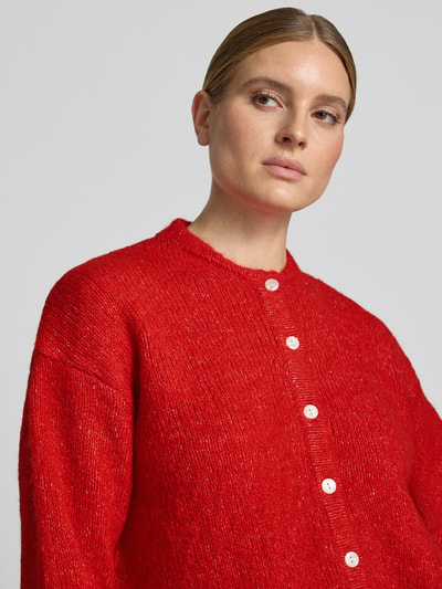 Frauenmodel trägt Relaxed Fit Strickjacke mit Woll-Anteil Modell 'Belablue' von ICHI in kräftigem Rot, weiße Knopfleiste, Nahaufnahme Oberkörper. Damen Strickjacke, elastischer Material-Mix, Rundhalsausschnitt, gerippte Bündchen.