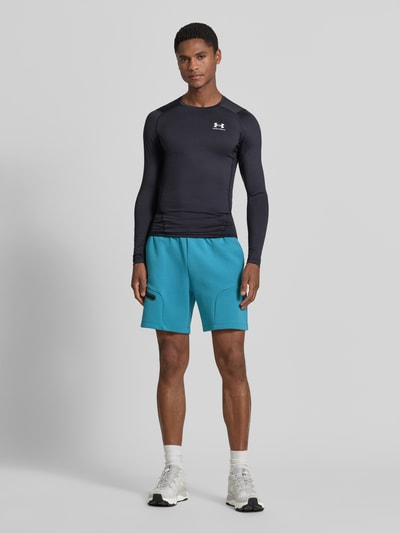 Męski model nosi szorty z kieszenią zapinaną na zamek błyskawiczny od Under Armour, mieszanka bawełny, krój regular fit, logo, elastyczny pas, szerokość w rozmiarze M: 39 cm, długość wewnętrzna nogawki w rozmiarze M: 18 cm, widok całej sylwetki z przodu.