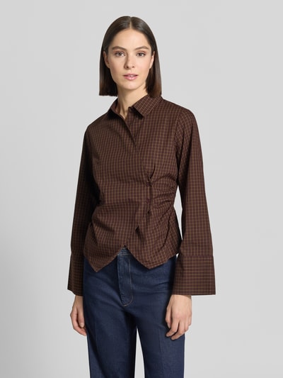 Frauenmodel trägt Bluse mit asymmetrischer Knopfleiste Modell 'Fenli' von Neo Noir aus reiner Baumwolle, taillierter Schnitt, Karomuster, Kimonoärmel, Farben Braun und Dunkelrot, Kentkragen, Ganzkörperansicht von vorne.